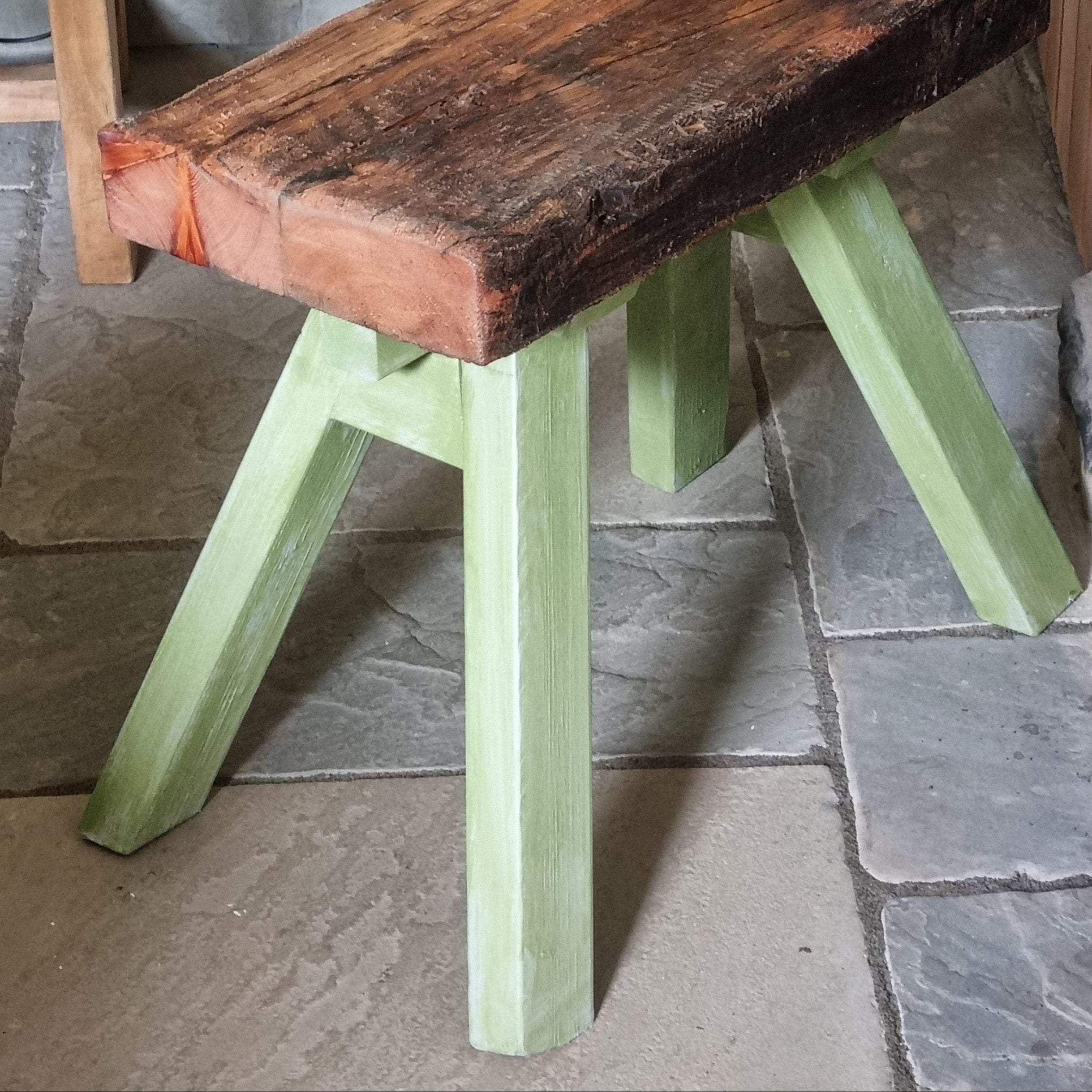 Green stool with wooden seat against a stone wall