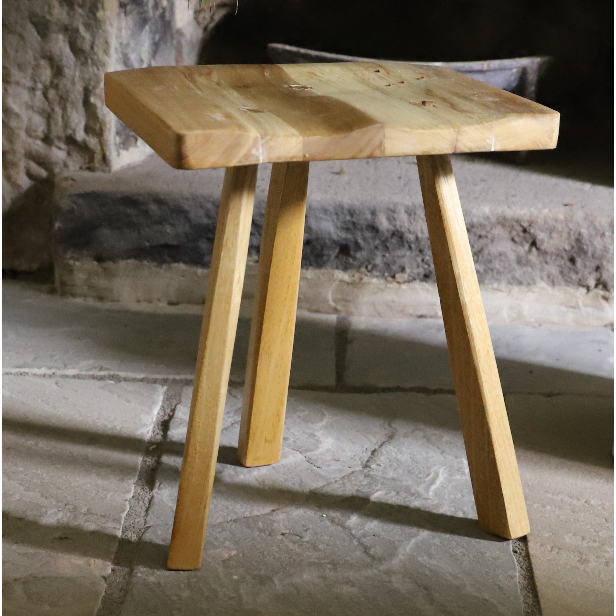 Wooden stool with a rustic design on a stone floor.