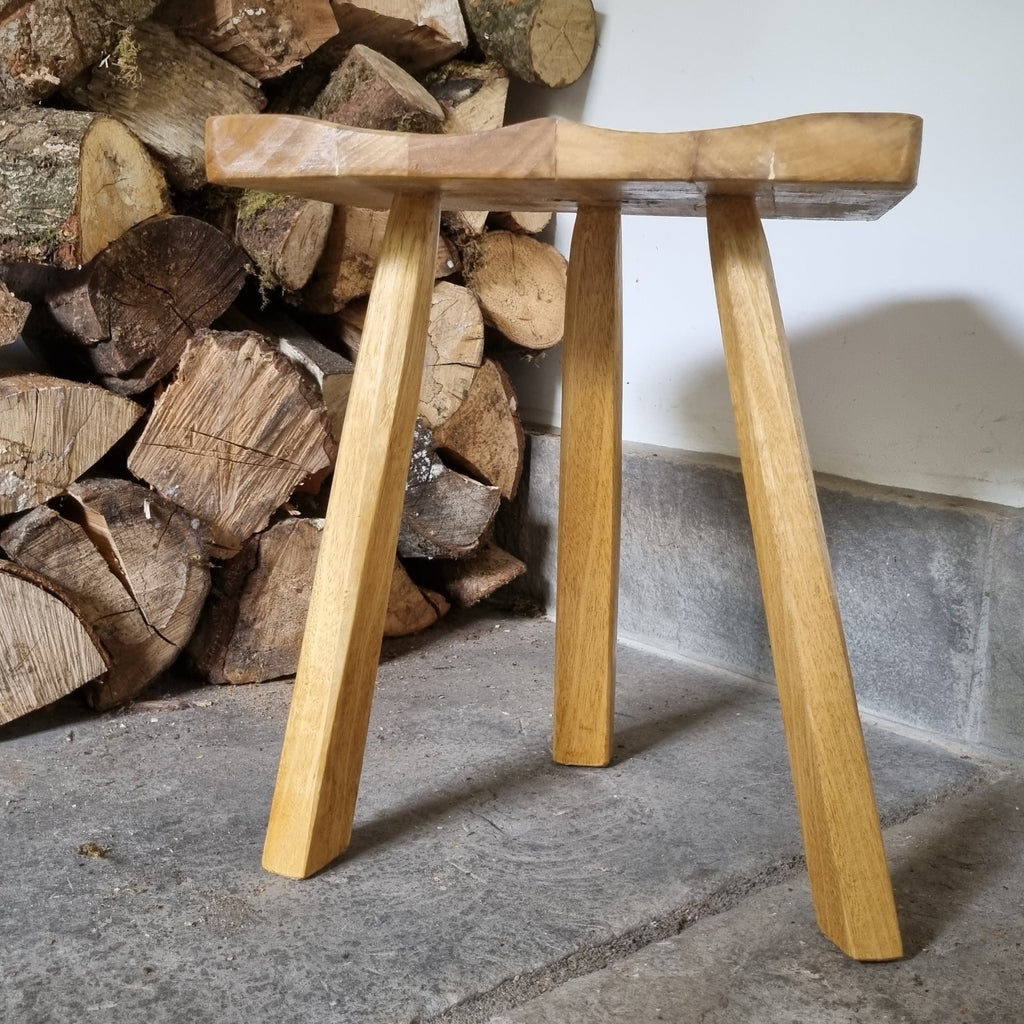 Wooden stool in front of stacked logs on a stone floor